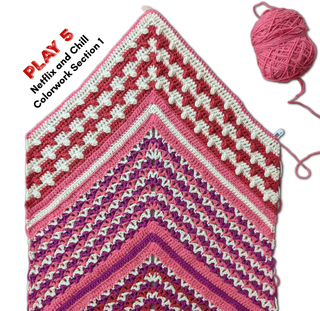 Partially finished shawl in pink, red, white, and purple yarn with visible colorwork detail; matching yarn ball included.