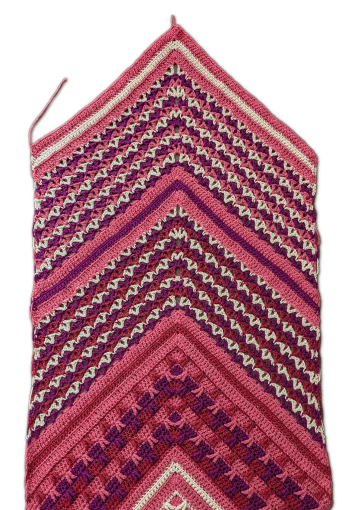 Chevron crochet blanket in pinks, purples, reds, and cream with textured geometric stitches and soft drape.