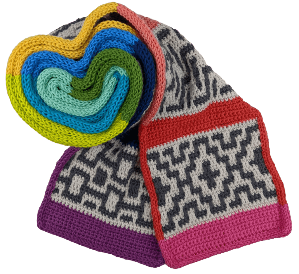 A hand-knit scarf with intricate patterns. The scarf features alternating sections of gray patterns on a cream background and colorful stripes. One end of the scarf is rolled into a heart shape, revealing layers of vibrant yellow, blue, green, and pink—perfectly complementing a Mosaic Crochet Hat. -Marly Bird