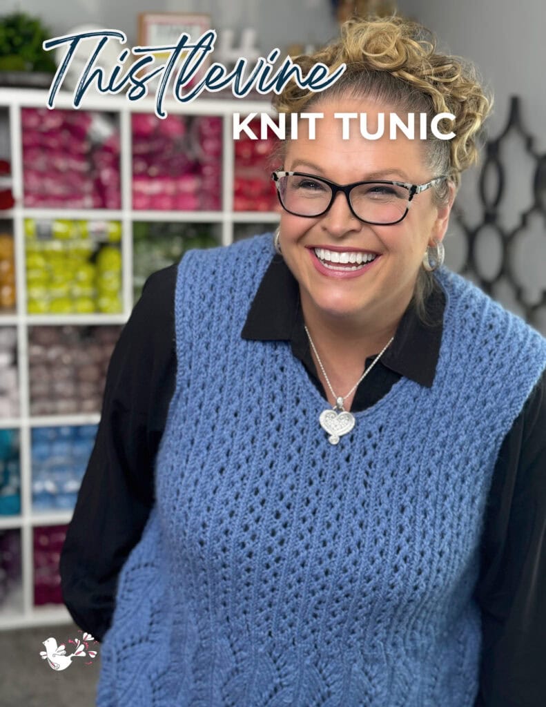 A smiling woman wearing glasses and a blue knit tunic stands in front of shelves filled with colorful yarn. Text reads, "Thistlevine Knit Tunic. -Marly Bird