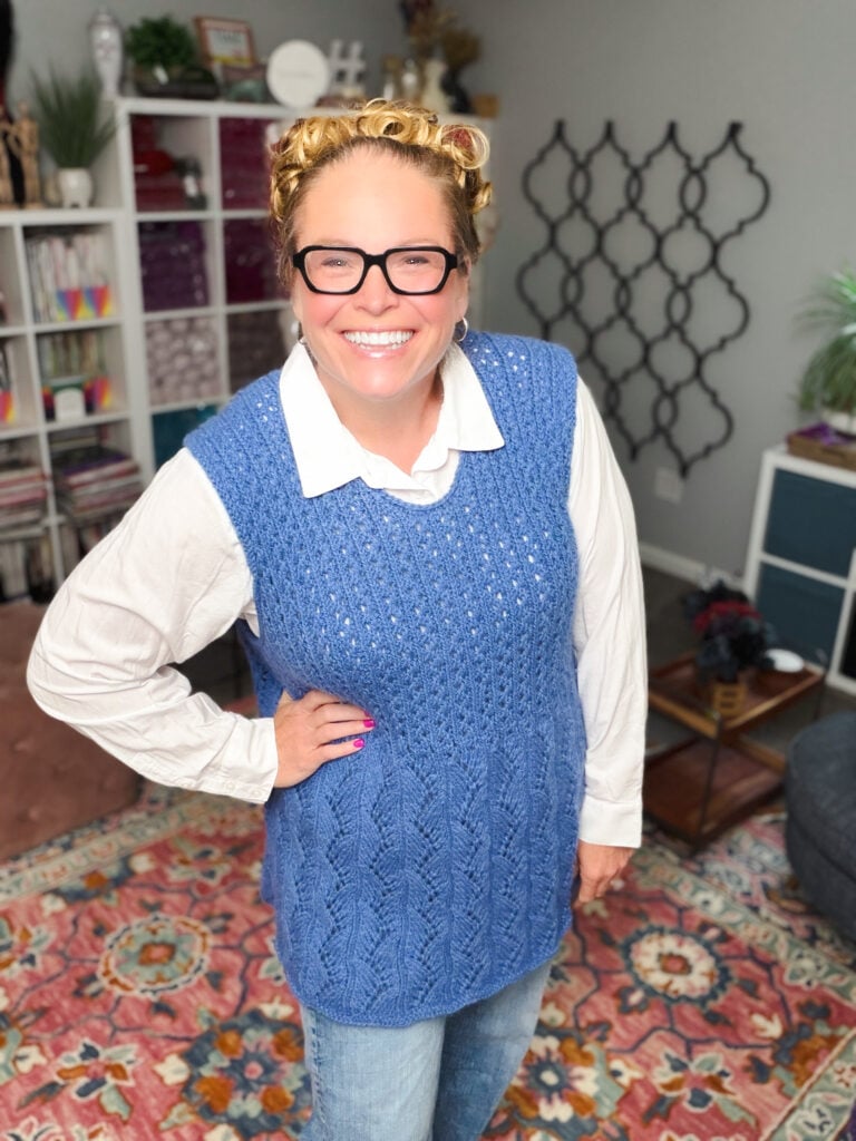 Person models a blue knit vest over a white shirt in a cozy, colorful room; texture and stitch detail of tunic pattern visible.
