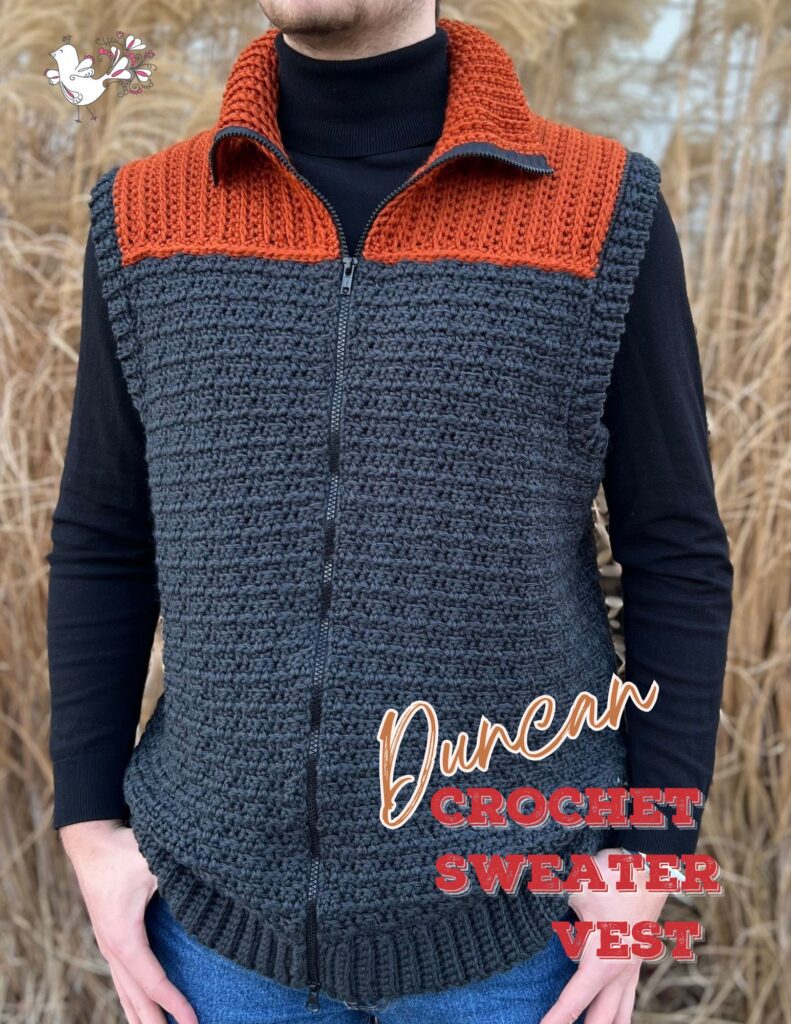 A person wearing a handmade crochet sweater vest that features a dark gray base with an orange collar. The vest has a full-length zipper and is modeled outdoors with a natural backdrop, perfect for the 2023 holiday season. -Marly Bird