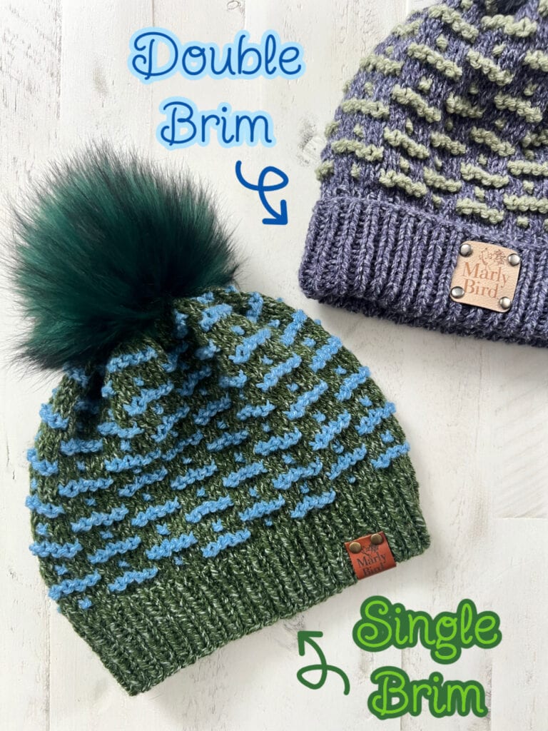 Two knit hats are displayed on a light surface. The top hat is purple with a tan label marked "Double Brim." The bottom, featuring a charming knit mosaic hat pattern in green and blue, has a fluffy pom-pom and a tan label marked "Single Brim." Both labels read "Marly Bird. -Marly Bird