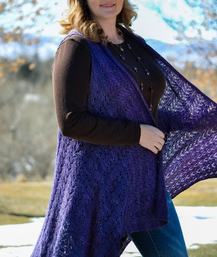 Purple open-front knit duster with textured stitches, worn over brown top and jeans, shown outdoors with trees and snow in background.