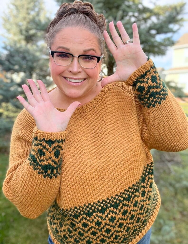 Woman modeling a yellow cropped pullover with green stranded colorwork, showing texture and fit outdoors among trees.