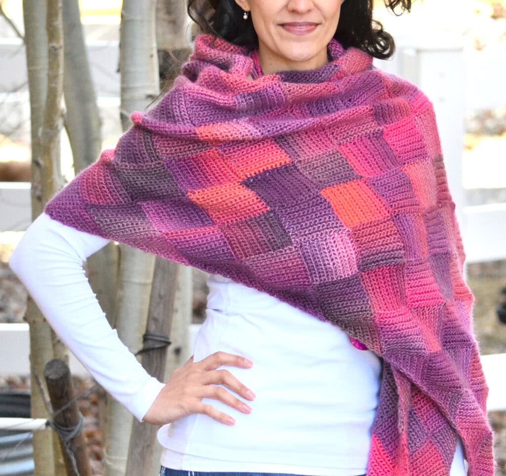 A woman models a vibrant entrelac crochet shawl in purples, pinks, and reds; detailed single crochet stitches are visible.