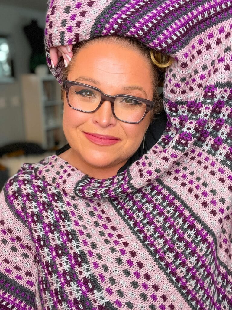 A Slip Stitch Shawl in purple, pink, and white is worn, showing off the textured pattern as it's draped playfully over the head.