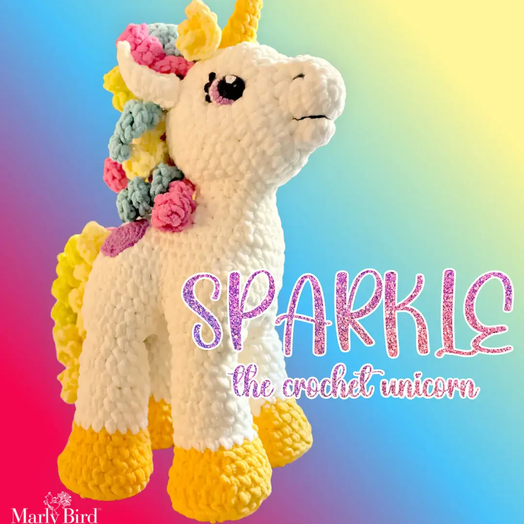 Crocheted unicorn amigurumi with white body, yellow hooves and horn, pastel mane on a gradient background. "SPARKLE" text above.