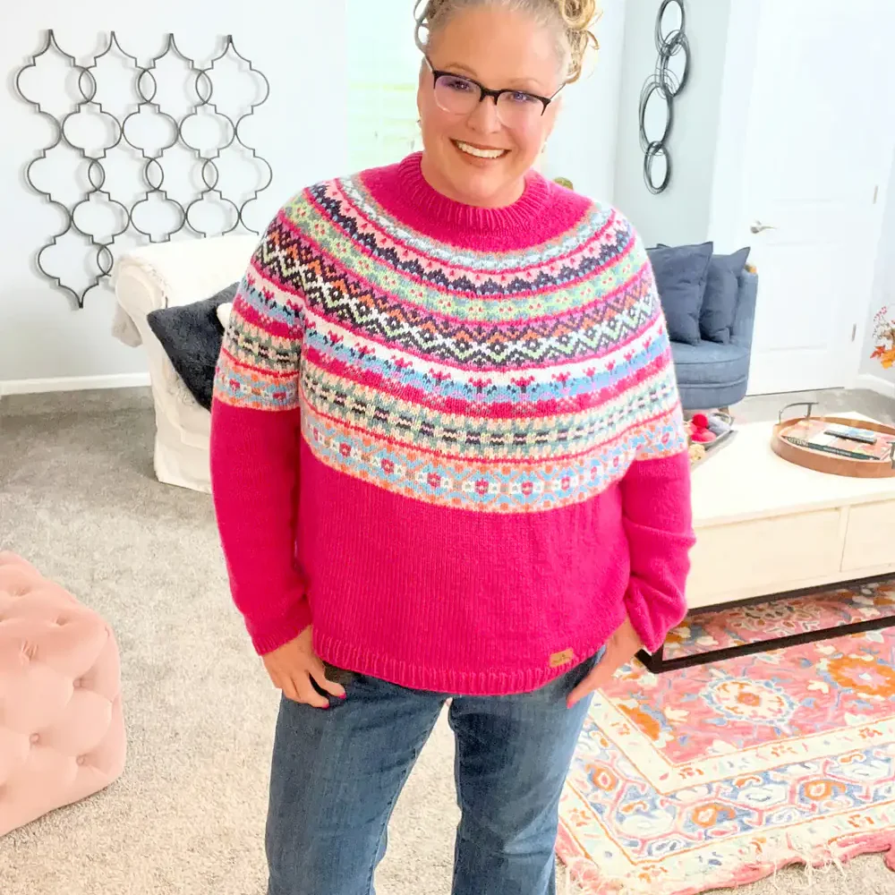 Bright pink hand-knitted sweater with colorful patterns, chunky texture, and neat stitches modeled in a cozy living room.