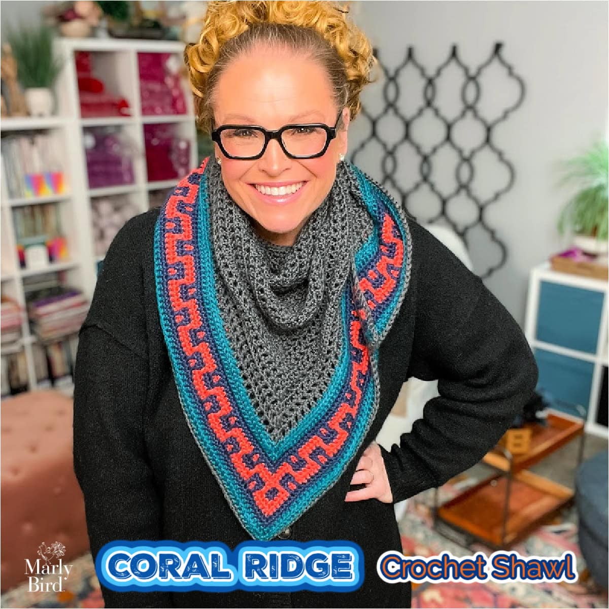 A person wears a crocheted triangular shawl featuring coral, teal, and gray patterns; texture and stitch detail are visible.