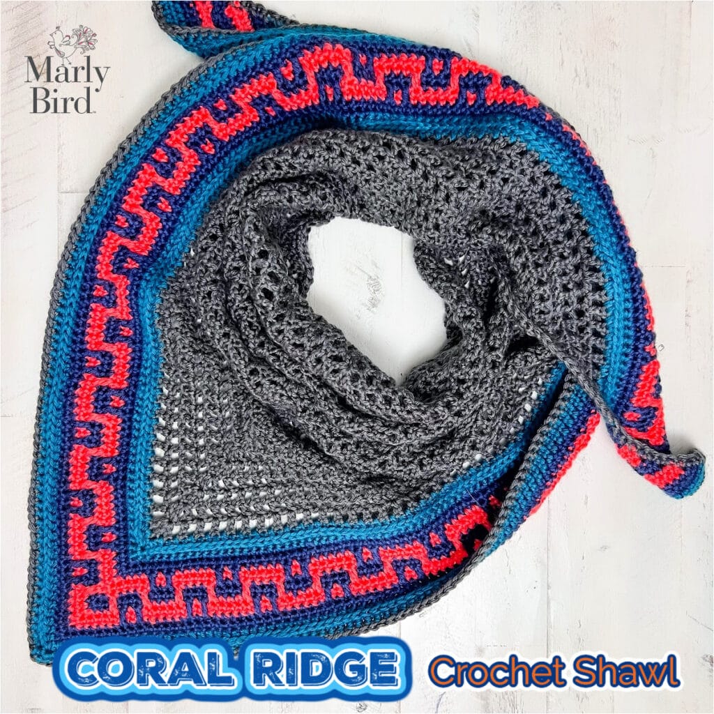 Coral Ridge free crochet triangle shawl pattern detail — gray crochet body with colorwork blue, red, and pink Greek-key colorblock border