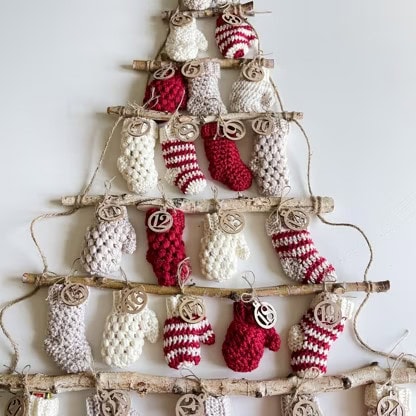 A tree made of sticks adorned with knitted mittens, wooden tags, and touches inspired by a crochet advent calendar. -Marly Bird