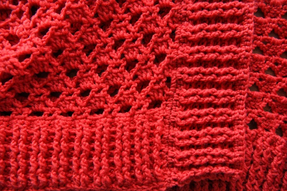 Red knitted fabric with open-lace stitches and ribbed sections, showing detail ideal for cardigan projects.