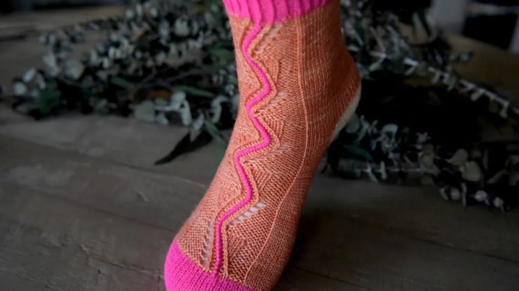 Orange knit sock with bright pink toe, heel, and cuff; vertical pink zigzag detail; shown worn, texture clearly visible.
